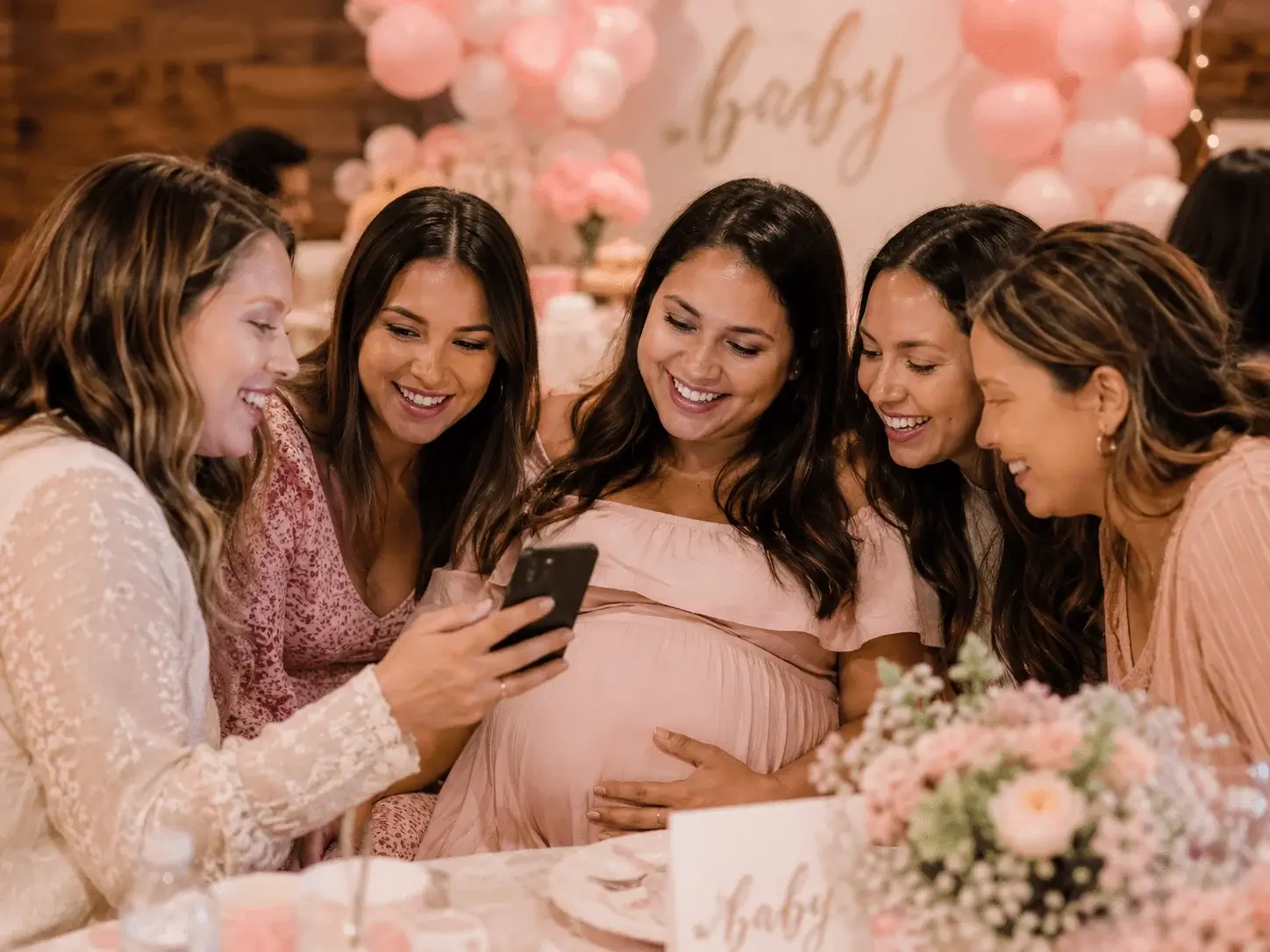 Friends gathered at baby shower sharing photos on a phone